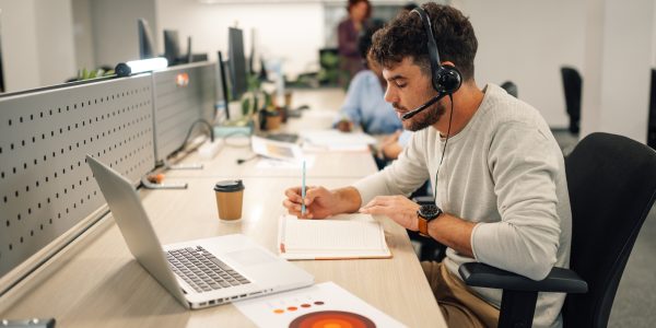 Customer services agent with headset writing notes in a call center