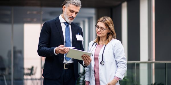 Pharmaceutical sales representative with tablet talking to doctor