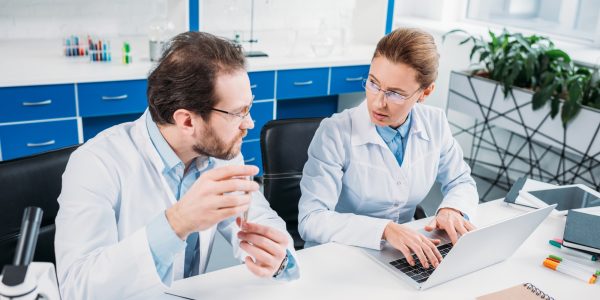 scientific researchers in white coats discussing work at workplace in laboratory